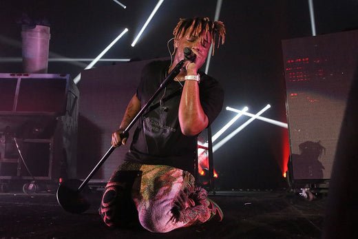 Juice Wrld on his knees on stage holding a microphone stand and singing into it