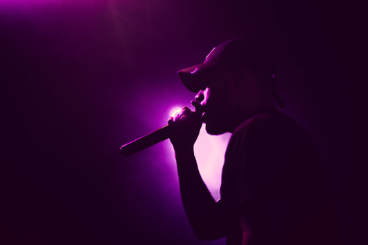 Man in a hat singing into a microphone in a dark spotlight room